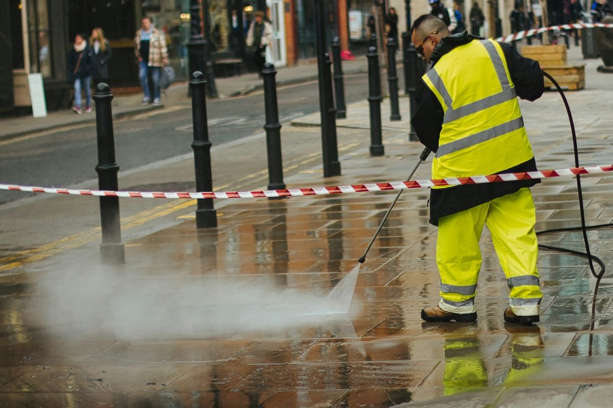 Operative in hi-vis pressure washing a pavement behind barrier tape